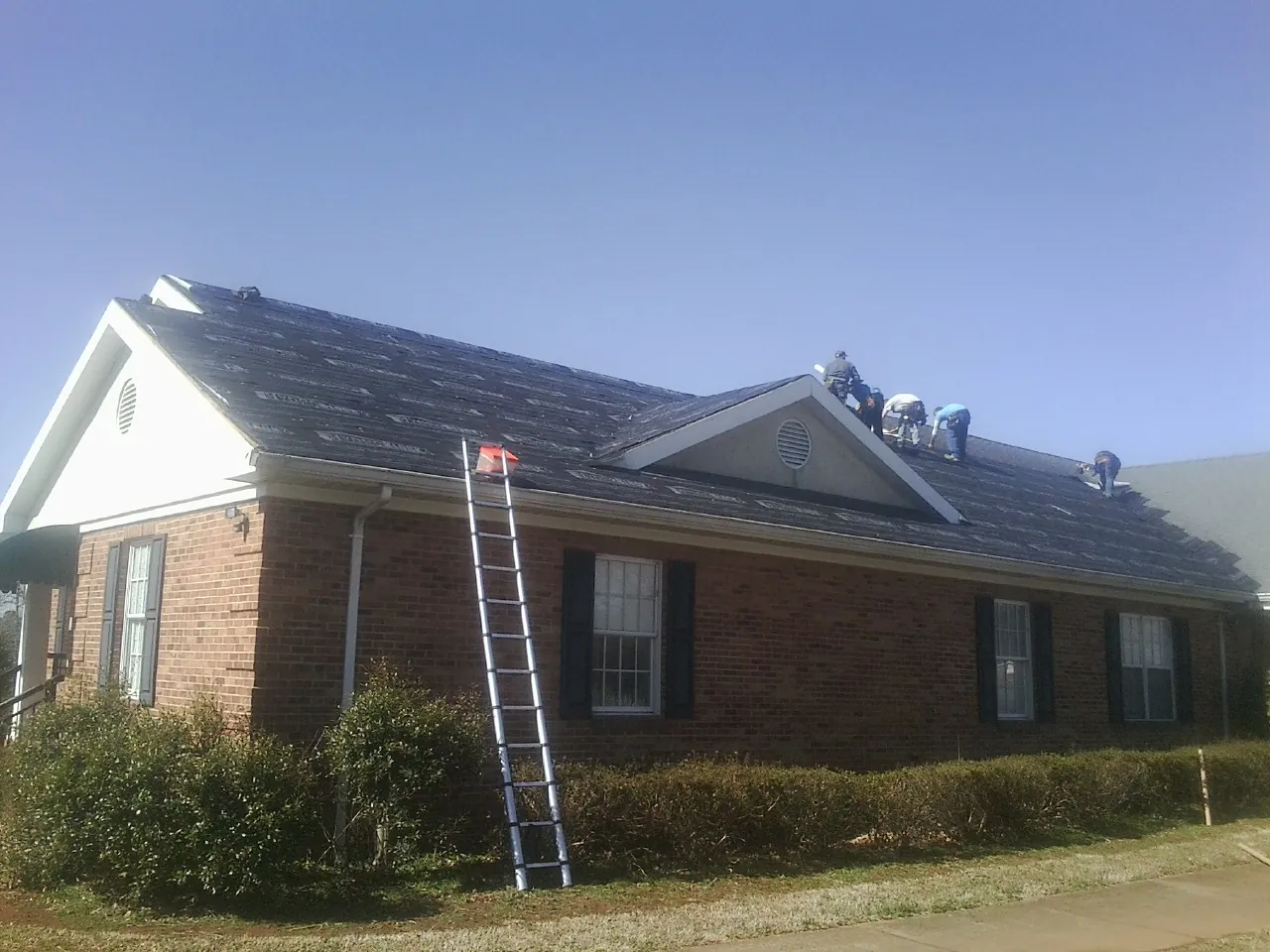Crew tearing shingles off a brick ranch roof with a ladder set — Metal Roof Repair work by our crew in Bolingbrook