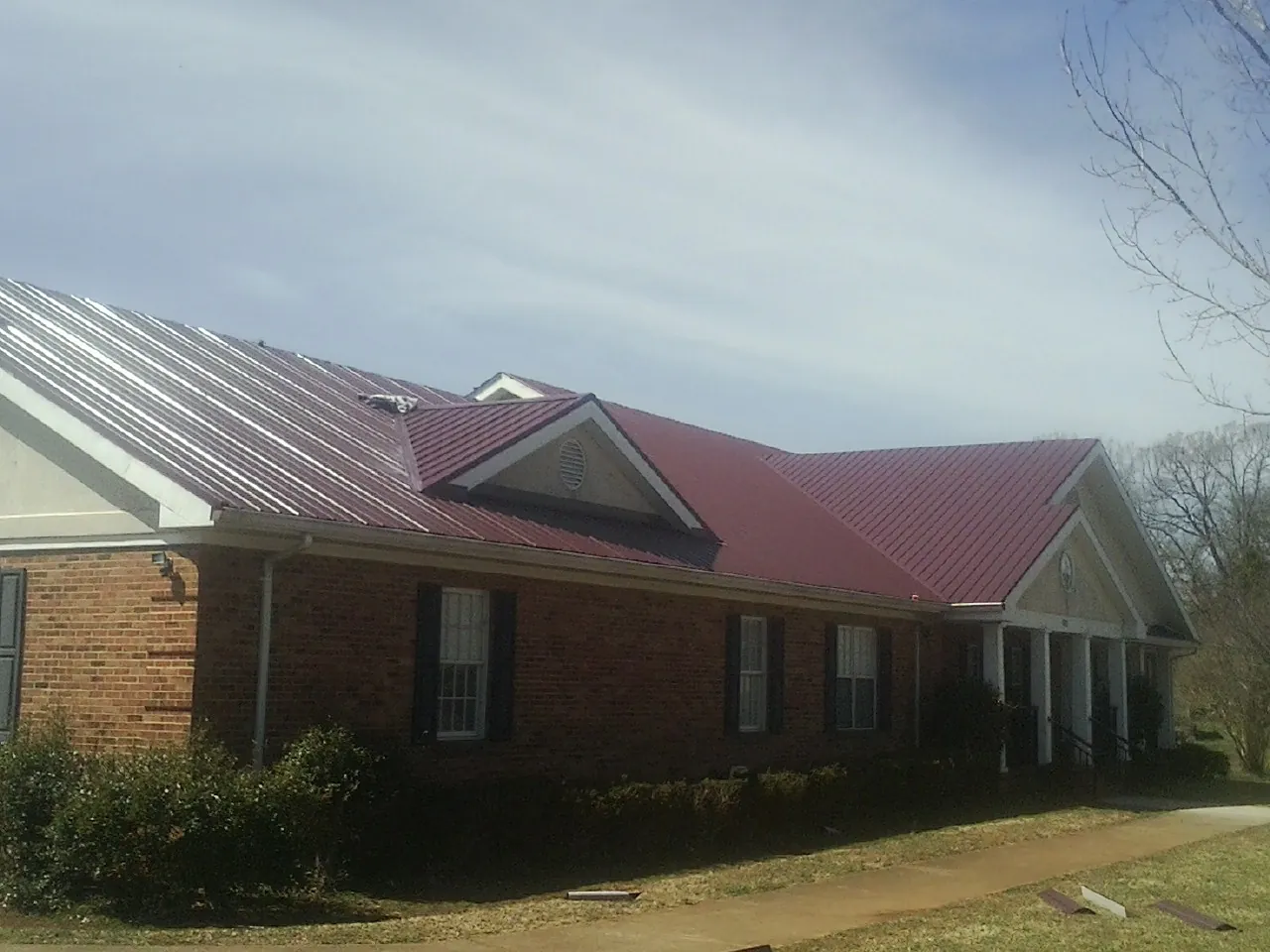 Red metal roof with gabled entries on a long brick building, from a Hail Damage Roof Repair job in Bolingbrook