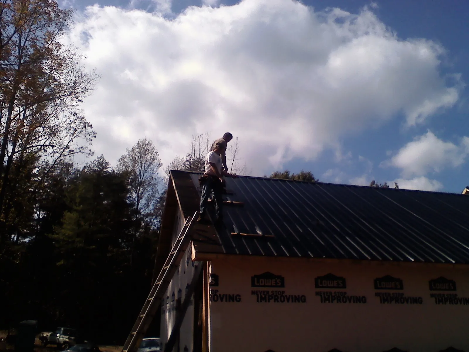 Roofer fastening dark metal panels high against a cloudy sky, from a Roof Inspection job in Bolingbrook